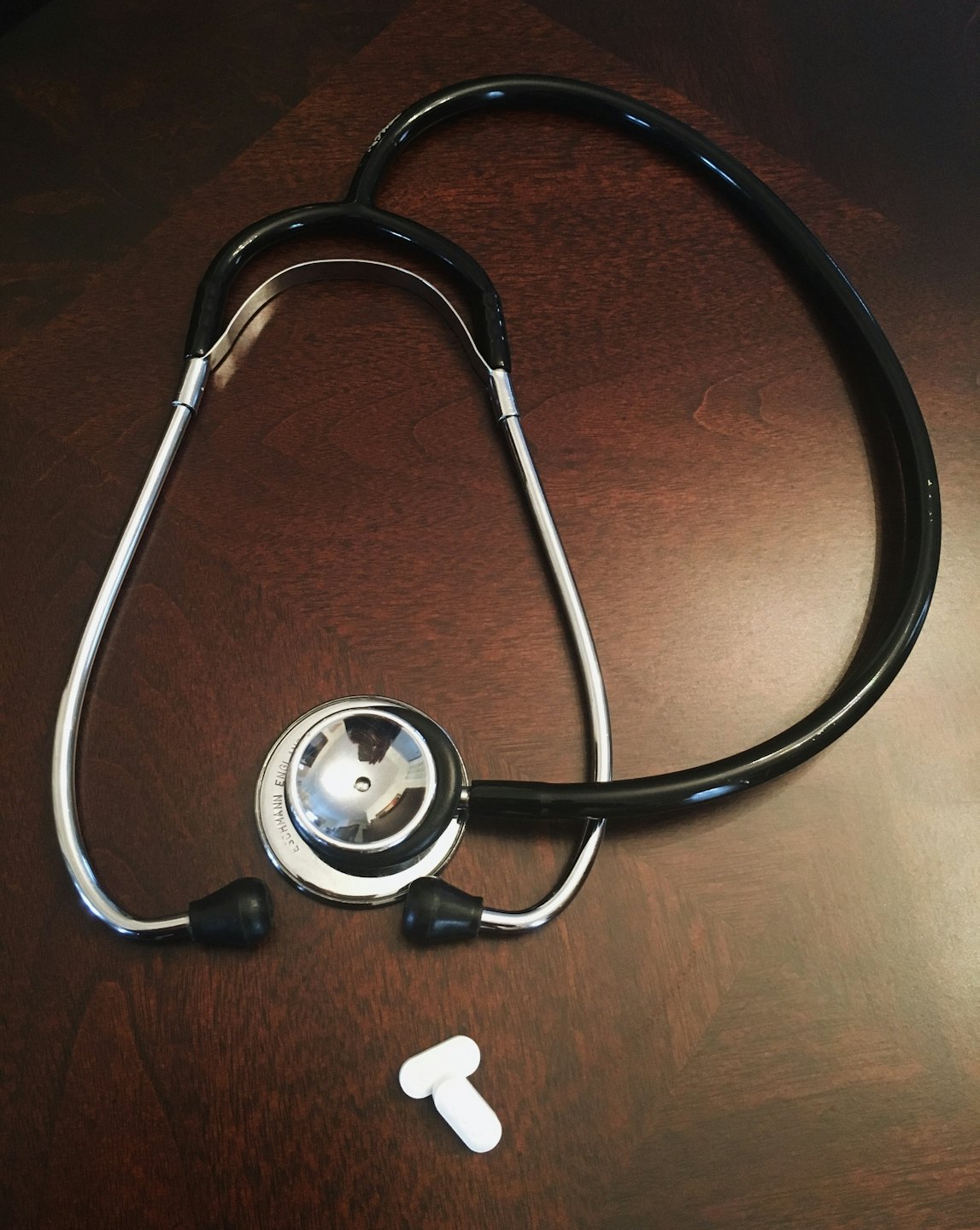 A stethoscope and two pills on a wooden table.